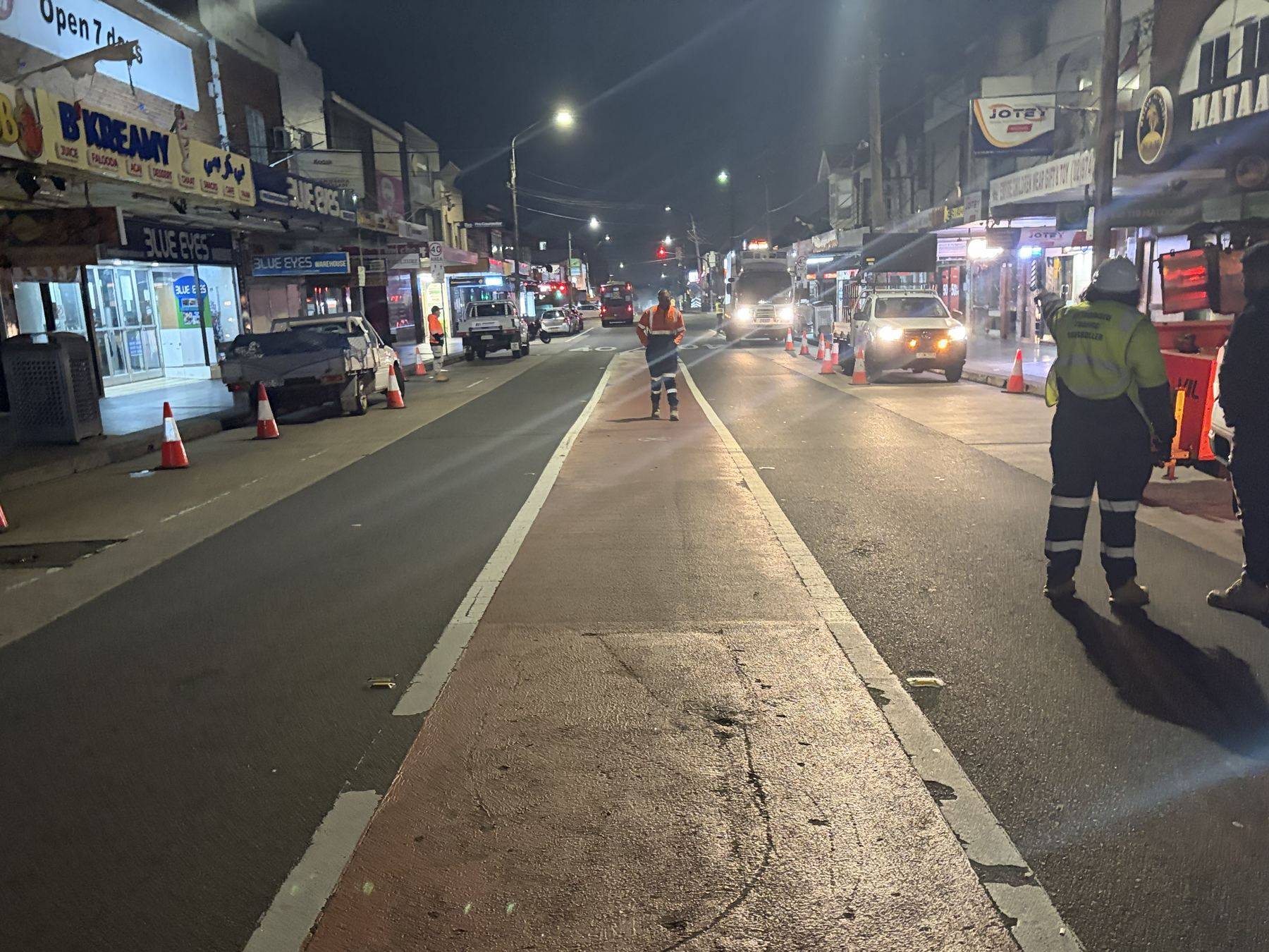 Haldon Street, Lakemba, under night traffic control, a lane coned off for borehole drilling with the shopfronts closed behind
