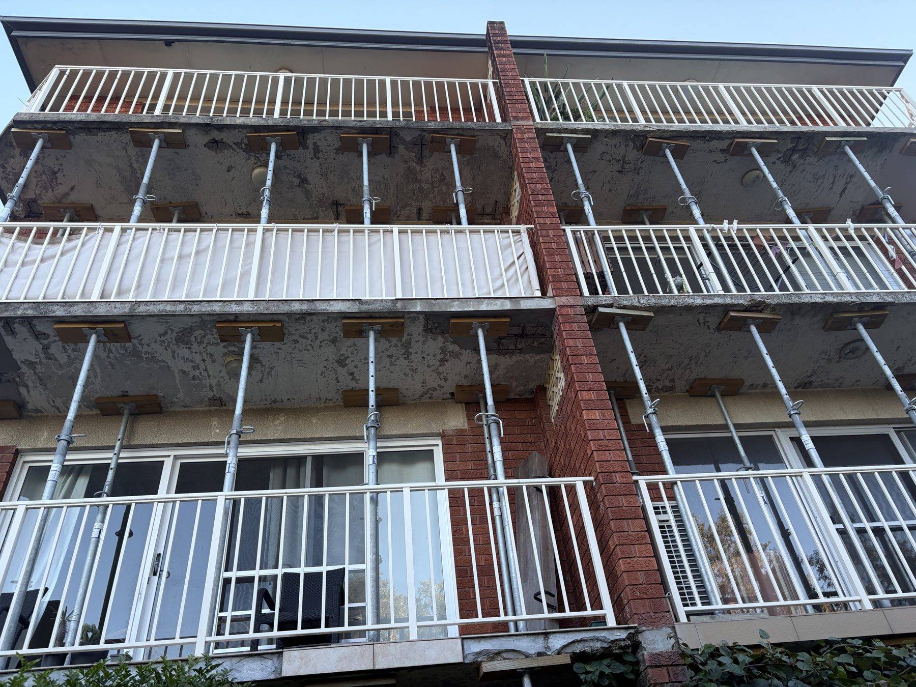 Rows of temporary steel props under the balconies of an occupied three-storey brick walk-up in Newport during the remedial investigation