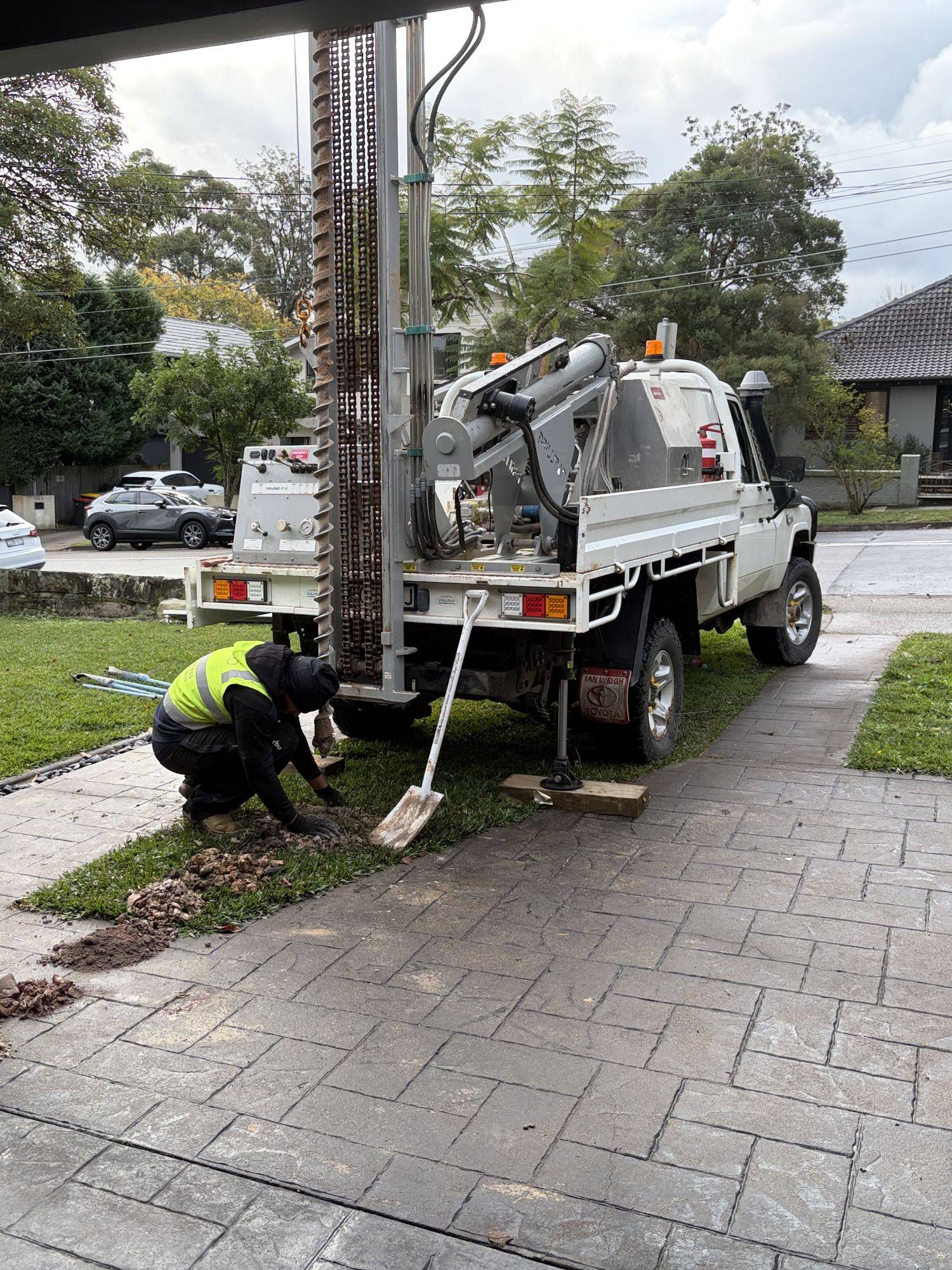 SFGEO 4WD drill rig set up on the front lawn of a suburban Sydney home with the engineer at the hole