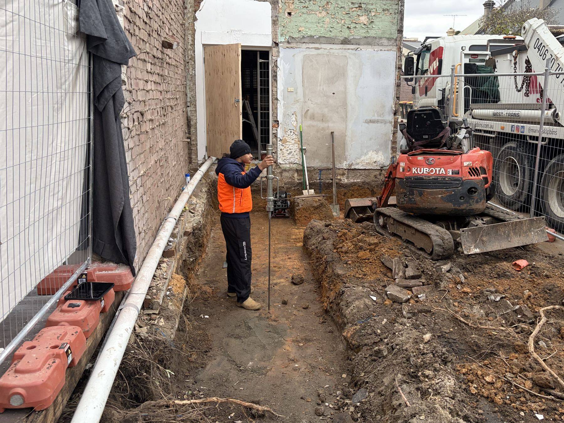 SFGEO engineer running a dynamic cone penetrometer in an open excavation beside a Newtown terrace before the pour