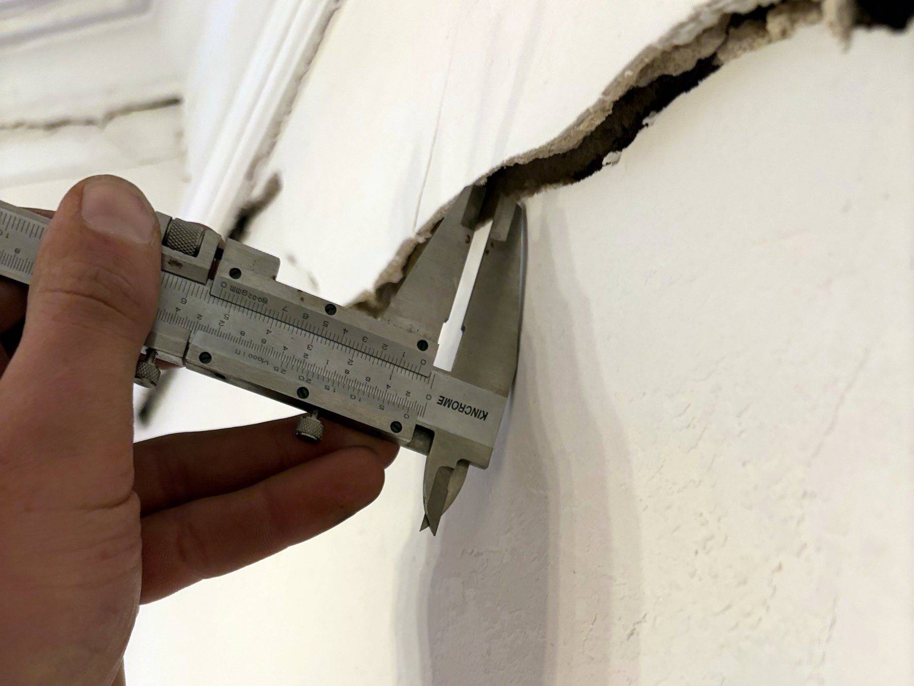 A stepped crack in a rendered wall measured with a vernier caliper during a dilapidation inspection in Naremburn
