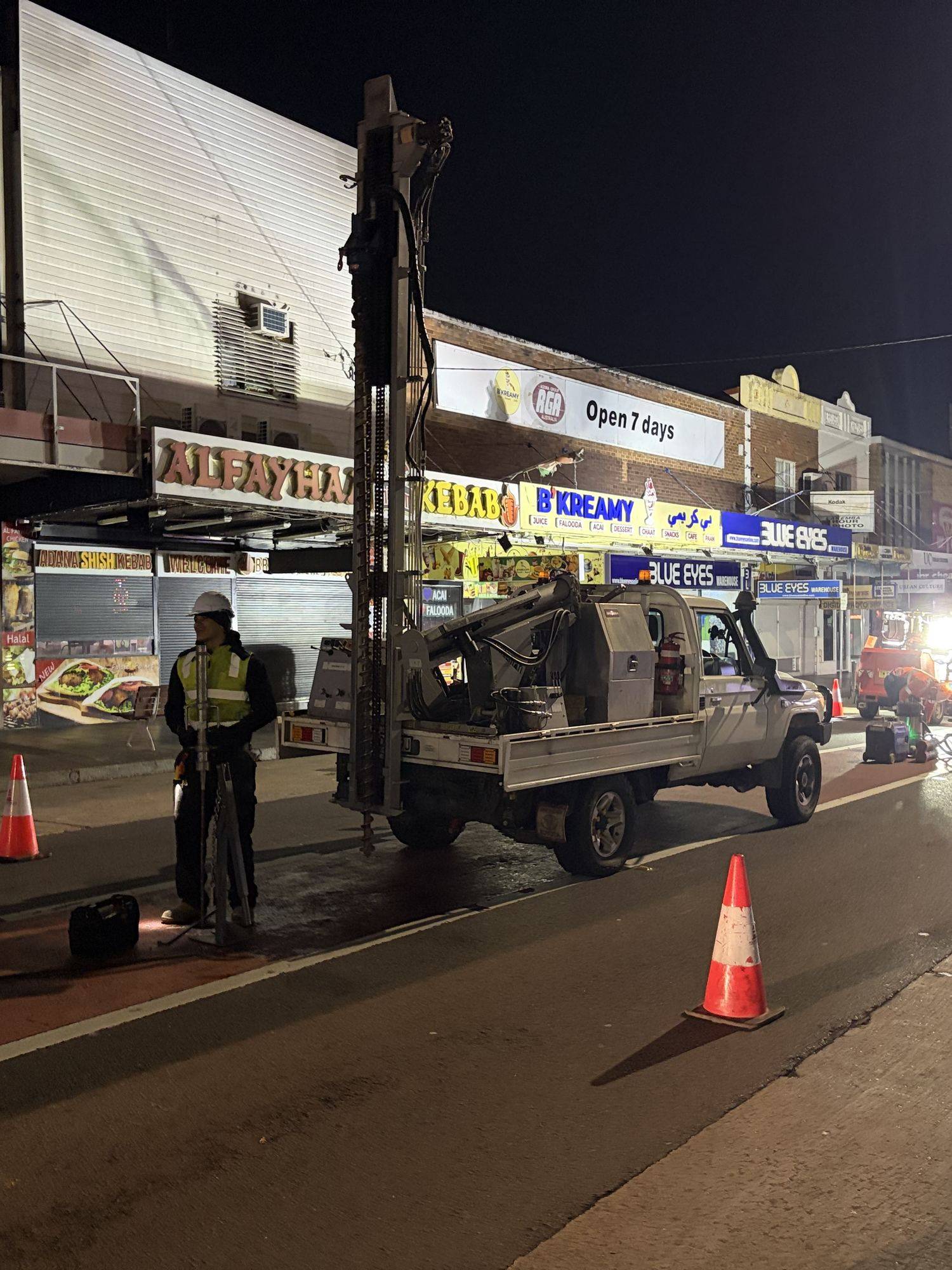 Drill rig with mast raised in a closed traffic lane during night works on a Sydney high street