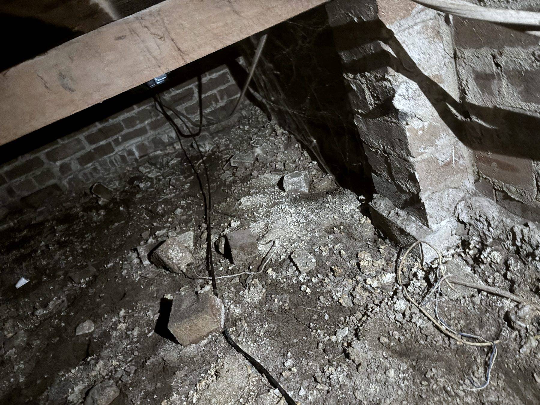 The undercroft of a Punchbowl house, a timber bearer over brick piers with rubble on the ground and barely room to crawl