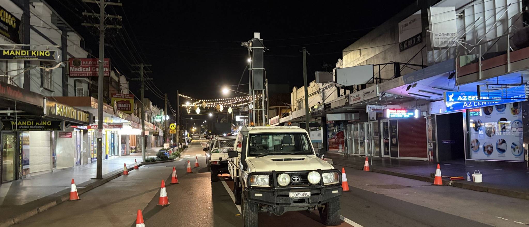 A Sydney high street closed under traffic control for overnight geotechnical works, shopfronts shut and the lane coned off